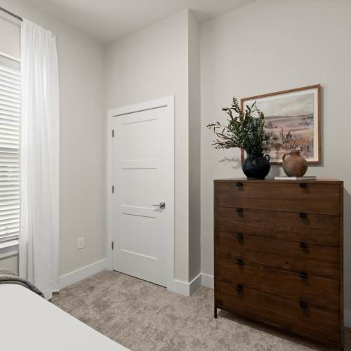 A neatly arranged bedroom with a bed, a dresser, and a window that provides a view outside at EVOQ East Cobb in Marietta, Georgia