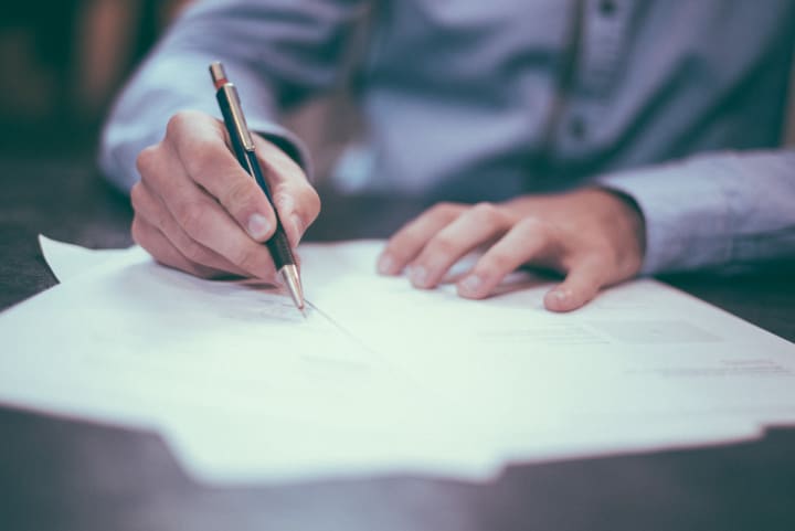 up close photo of hands doing paperwork, signing a document with a pen