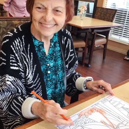 A resident smiling and coloring at Oxford Glen Memory Care at Grand Prairie in Grand Prairie, Texas