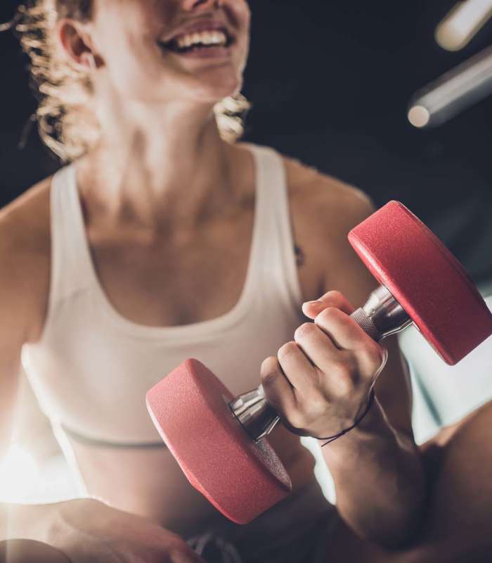 Woman smiling while lifting a red dumbbell in a fitness center at Jordache Park Apartments in Spencerport, New York