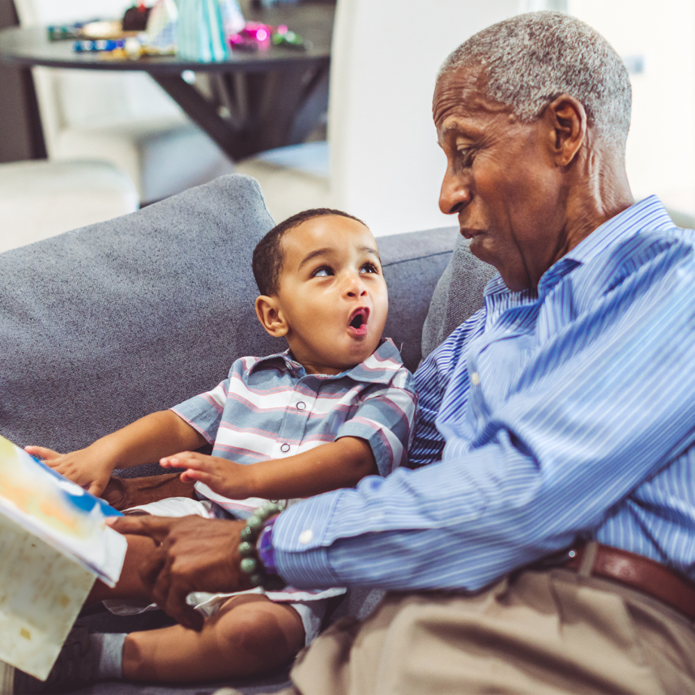 A elderly gentleman reading a book with a young child at Harbor Cove Memory Care in Hilton Head Island, South Carolina