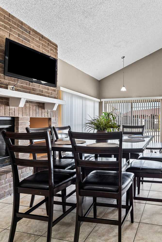 Dining area with black chairs, round table, and a brick fireplace with a TV above at Towne East Village Apartment Homes in Converse, Texas