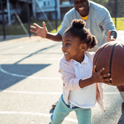 A father and daughter playing basketball on a court at The Village at Whitehurst Farm in Norfolk, Virginia