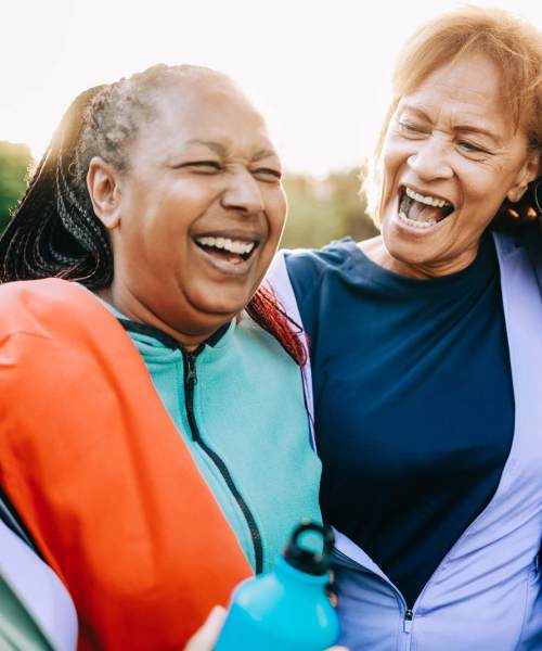 A couple of residents laughing outside near a park at Athens Vista Senior Apartments in Los Angeles, California