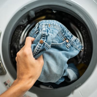A man's hand placing pants into the washer in an apartment home at Mariposa at River Bend in Georgetown, Texas