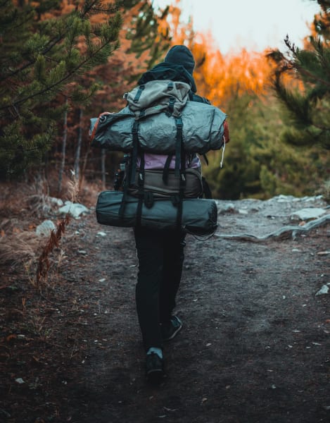 a backpacker hikes up a hill with a large pack and bundle on their back