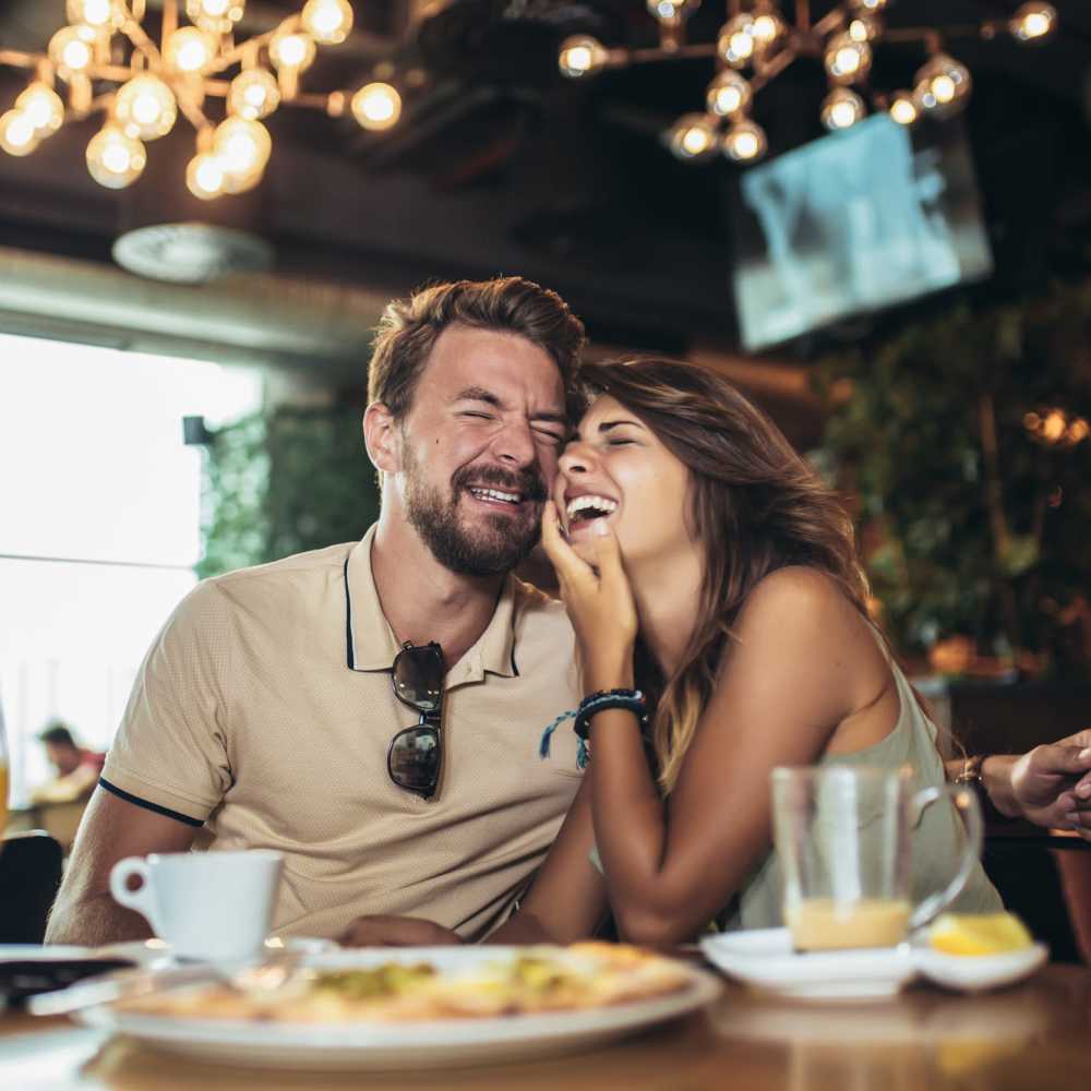 A couple share a joyful moment, laughing together at a table filled with delicious food near Park Manor in Lebanon, Oregon