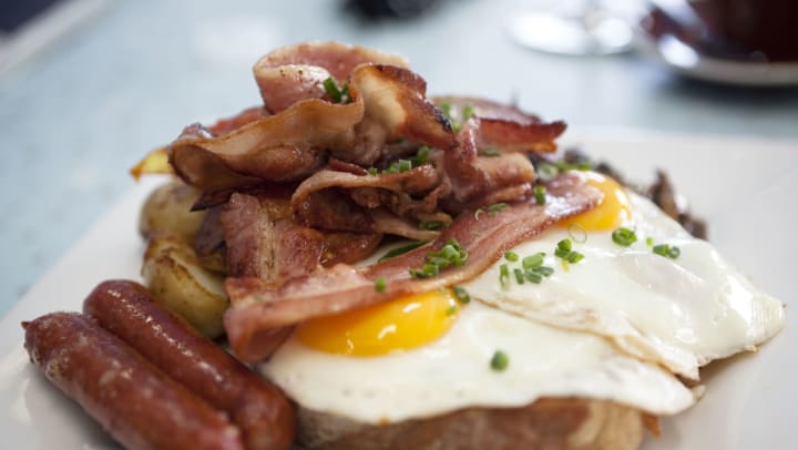 Two fried eggs and ham piled on top of toast with sausage and potatoes on the side. 