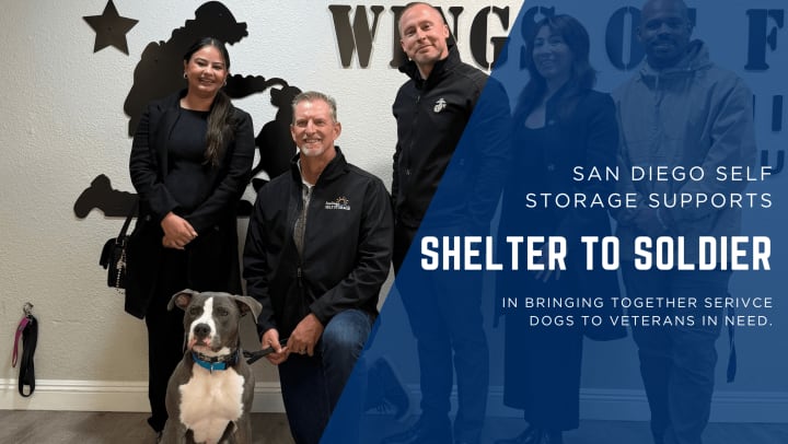 San Diego Self Storage team members posing with Bruno, a service dog in training, at the Wings of Freedom Training Campus with Shelter to Soldier branding in the background.