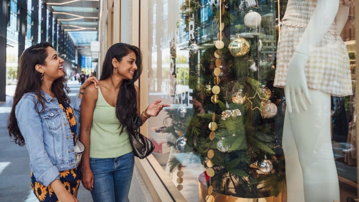 Two women looking through a window at a shop display of Christmas decorations. 