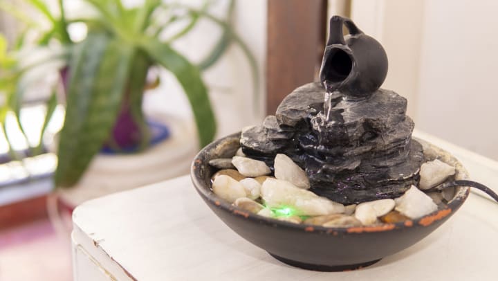 Small tabletop fountain features a pitcher on its side pouring water down a small stack of rocks.