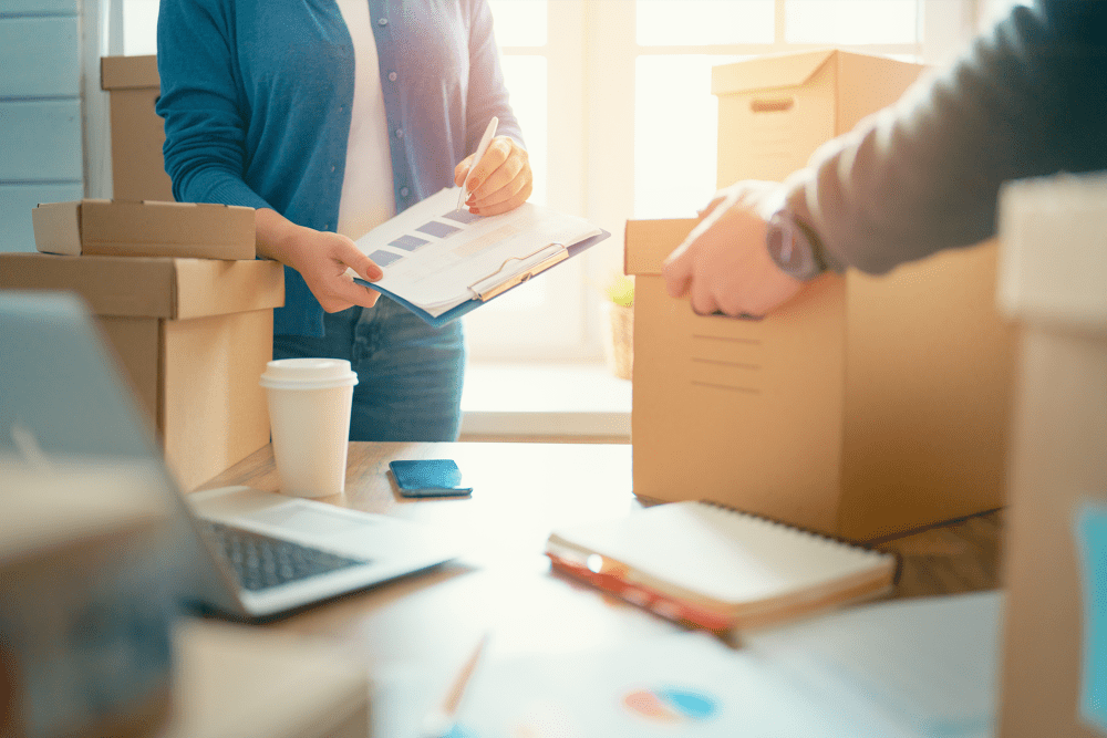 Woman holding a clipboard and man lifting a box from a table with business papers at A-American Self Storage in Denver, Colorado