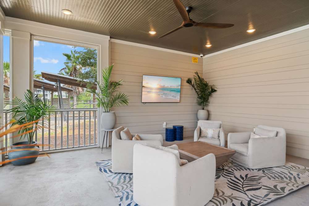Screened in outdoor lounge with television and ceiling fan at Pier Park Crossings Apartments.