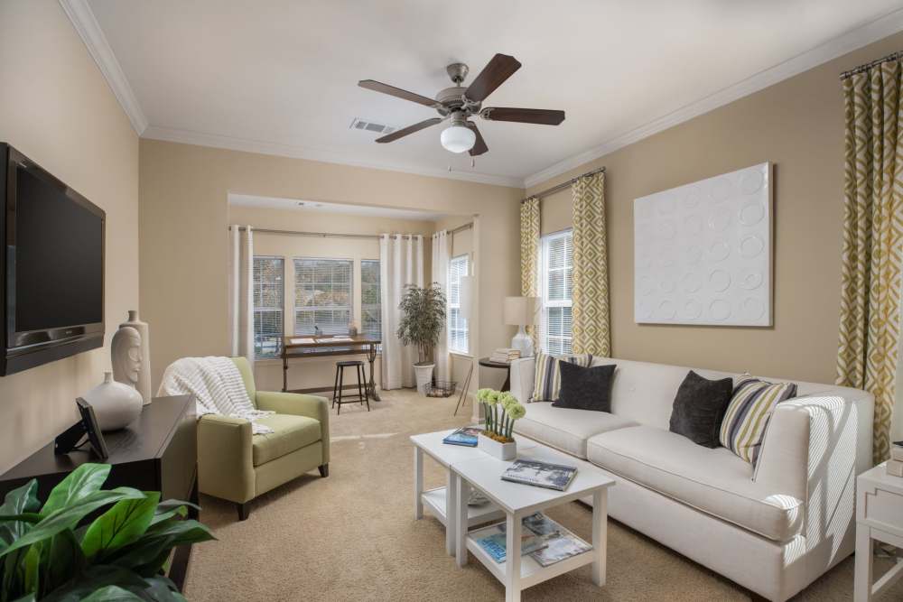 Apartment living room with carpeted flooring, white sofa, and sunroom at Wembly at Overlook in Macon, GA.