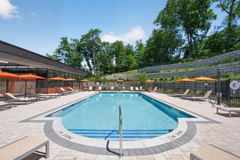 Outdoor swimming pool with lounge chairs and umbrellas at Eagle Rock Apartments at Woodbury in Woodbury, New York