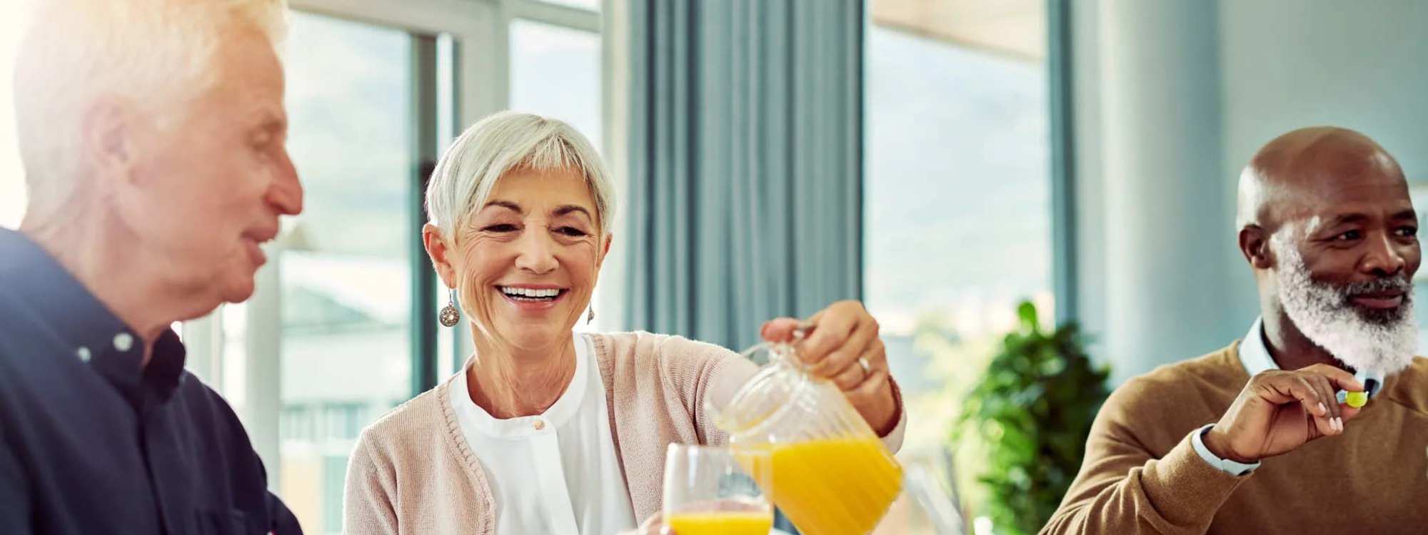 a woman smiling and pouring orange juice into a cup with two men smiling