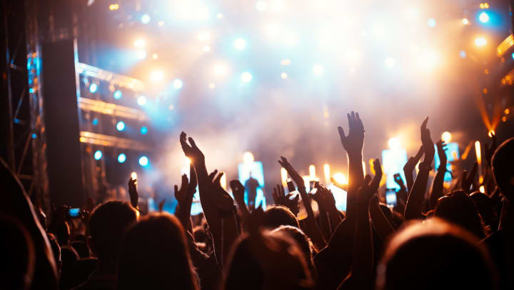 The crowd at a music concert watches the brightly illuminated stage. 
