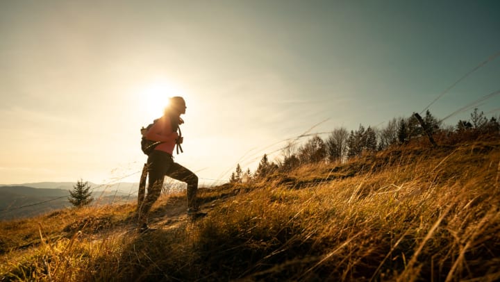 Silhouette of woman wearing backpack hiking on mountain
