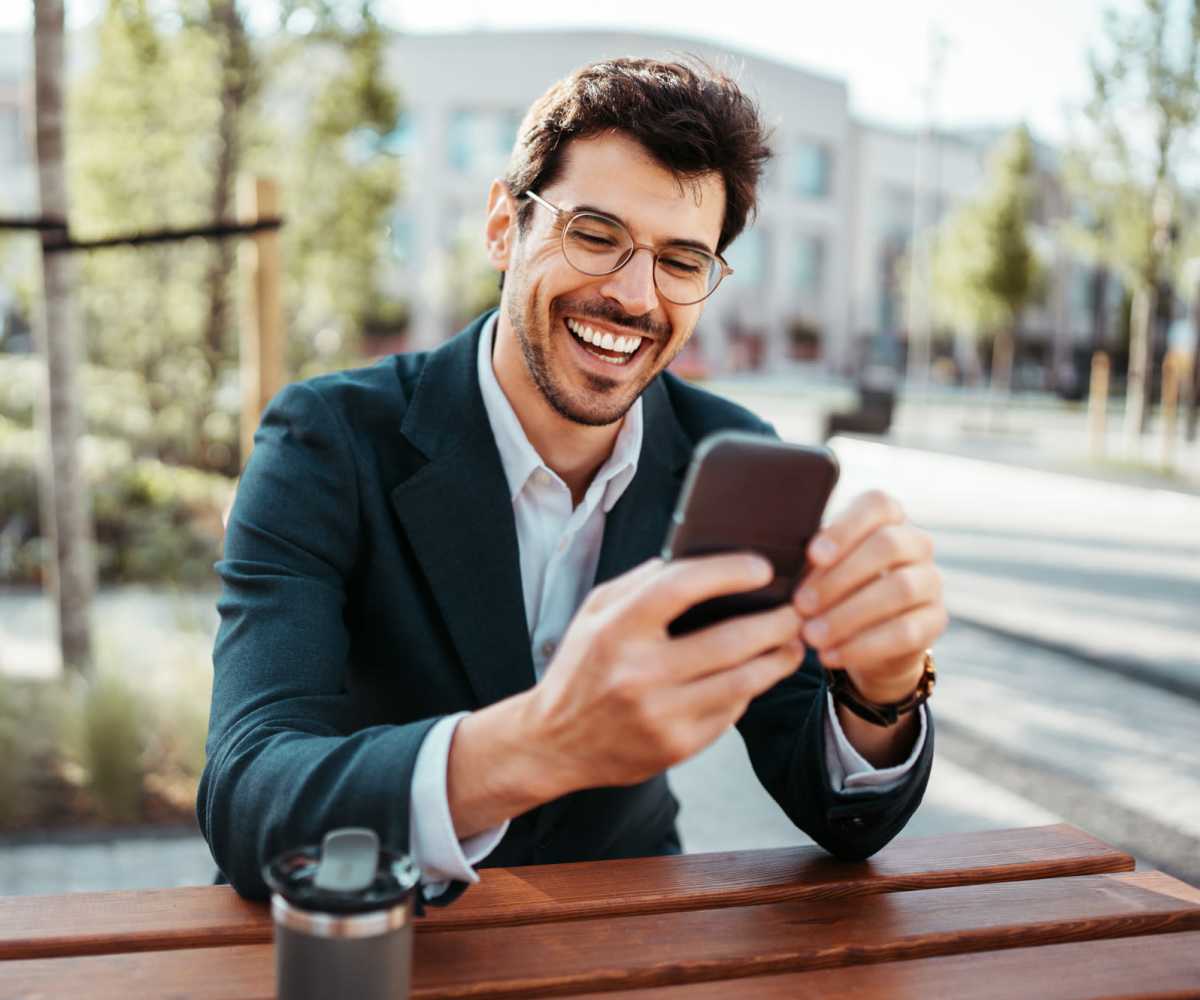 Man smiling while using smartphone at outdoor table near Midtown Exchange Apartments in Minneapolis, Minnesota