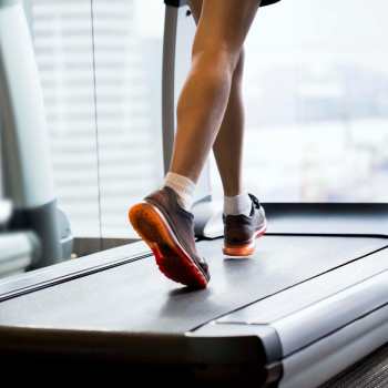 Person jogging on treadmill in modern gym with large windows and city views at South Oak in Ames, Iowa