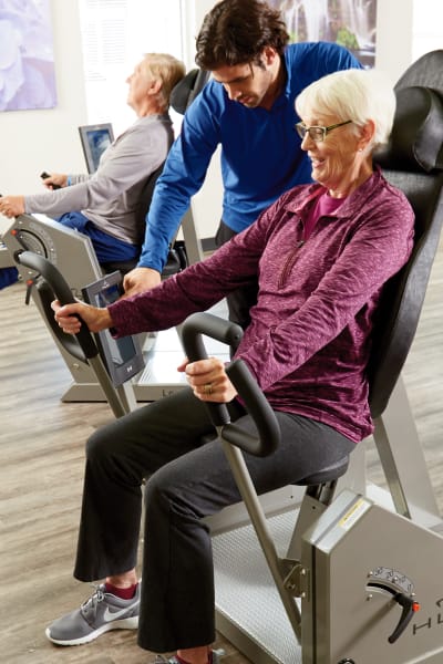 Gym instructor assisting a resident on a workout machine at Quail Park at Shannon Ranch in Visalia, California