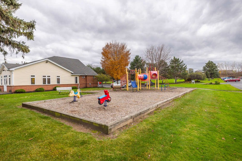 A colorful playground sits on a gravel patch surrounded by green grass at Greece Commons Apartments in Rochester, New York