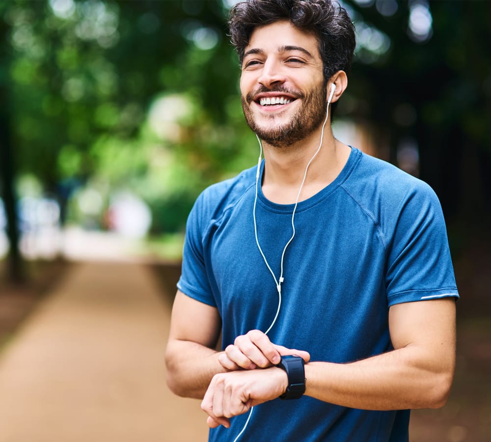 A man smiling in a park while touching his watch near Park at Kingsview Village in Germantown, Maryland