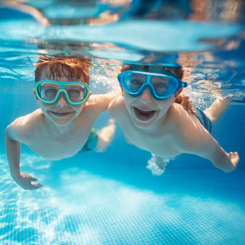 Two kids wearing googles and smiling underwater in the pool at  The Crossing at Palm Aire Apartment Homes in Sarasota, Florida 