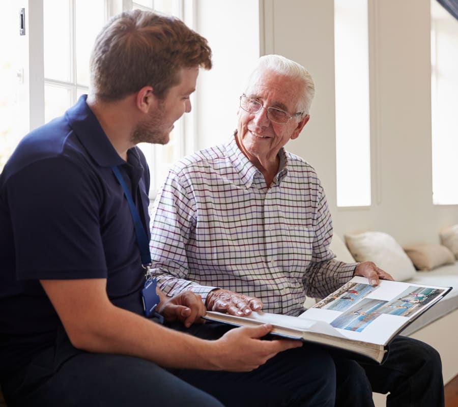 Resident looking at photo album with staff  at The Arbours at Linden Pointe in Winnipeg, Manitoba