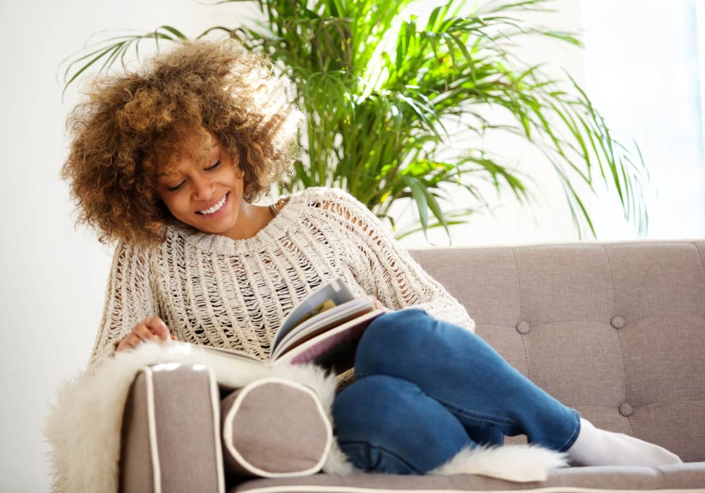 Resident relaxing on her couch while she reads a book at The Park at Ashford in Arlington, Texas