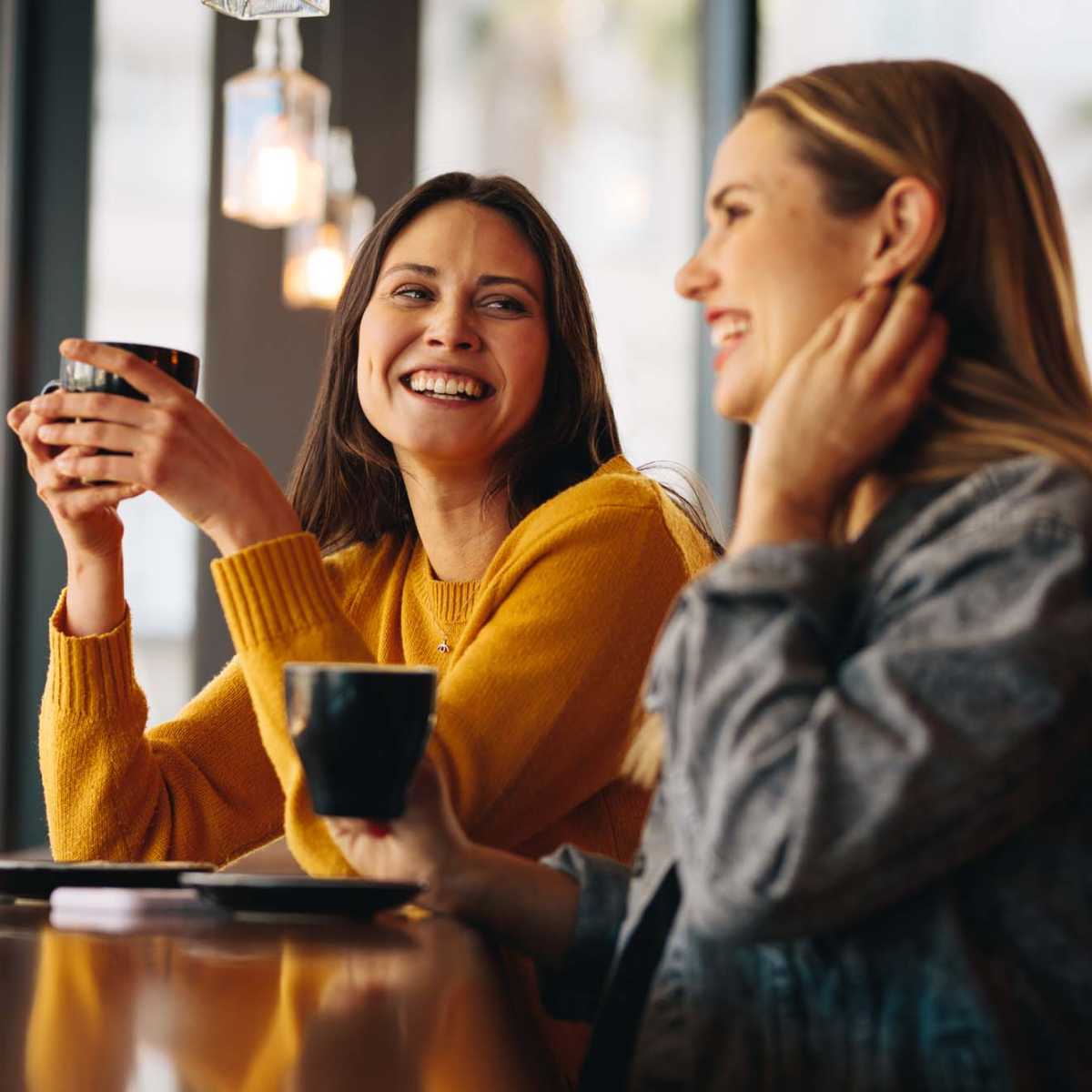 Two women smiling and enjoying coffee at a modern wooden counter with pendant lighting at Stevens Creek Commons in Augusta, Georgia 