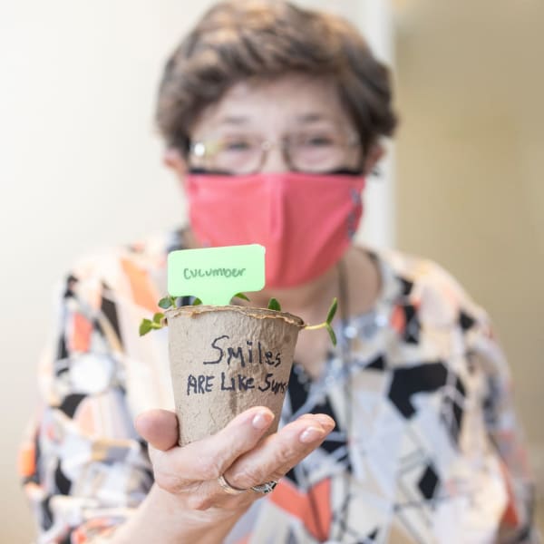 Resident wearing a mask holding a plant up at The Madison Senior Living in Kansas City, Missouri