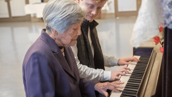 a senior lady playing piano with her caregiver