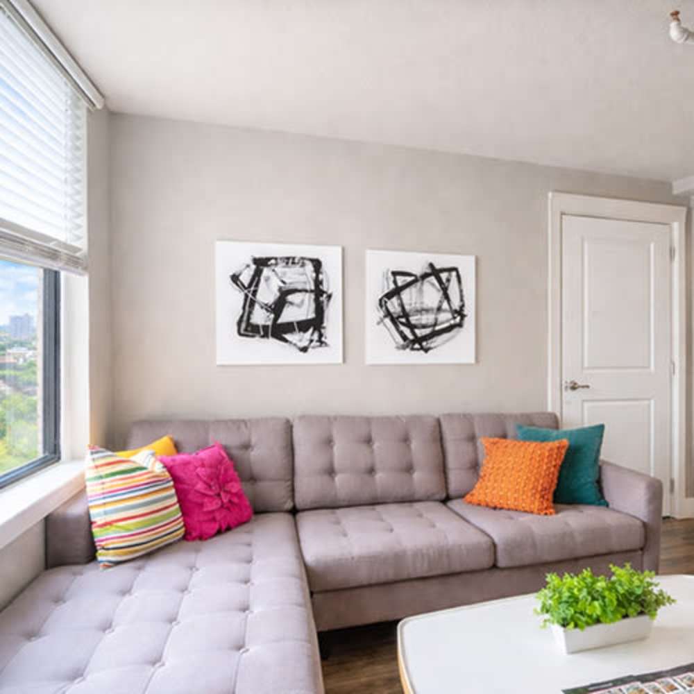 Bright living room with a gray sectional sofa, colorful pillows, and modern artwork on the walls at Flats on Fifth in Louisville, Kentucky