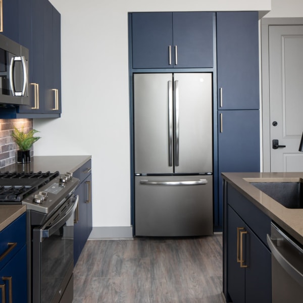 Townhome kitchen with hardwood floors, stainless steel fridge, and dark blue cabinets at Bellrock Sawyer Yards in Houston, Texas