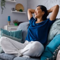 A smiling woman with her hands resting behind her head on her couch at The Courts of Avalon in Pikesville, Maryland