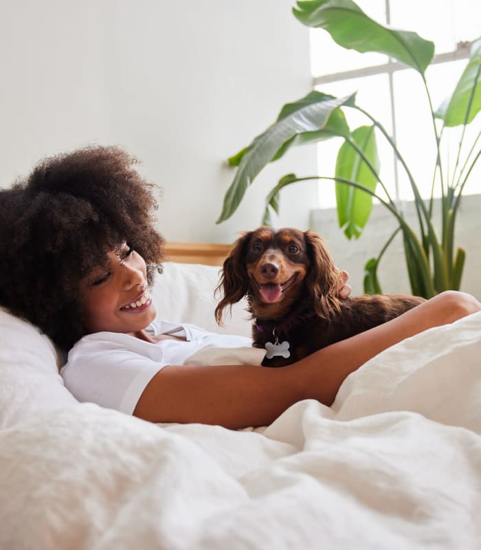 Smiling resident and her puppy relaxing in bed in their new home at Mission Rock at San Rafael in San Rafael, California