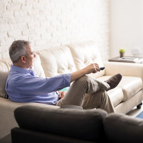 A resident  holding a remote and watching a TV at Ben Moreell in Norfolk, Virginia