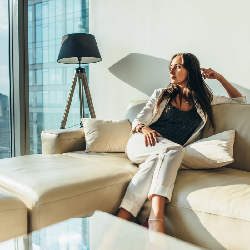 Resident relaxing on a plush cream-colored leather couch in her apartment home at The Meridian in Los Angeles, California