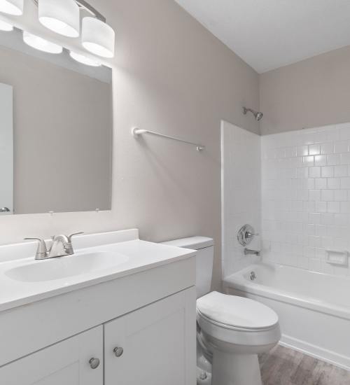 Bathroom with white vanity, mirror, toilet, and bathtub with white tile surround at Belmont Gardens in Pensacola, Florida