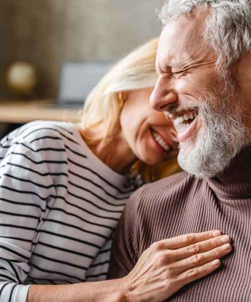 An elderly couple in their living room laughing togther at Athens Vista Senior Apartments in Los Angeles, California