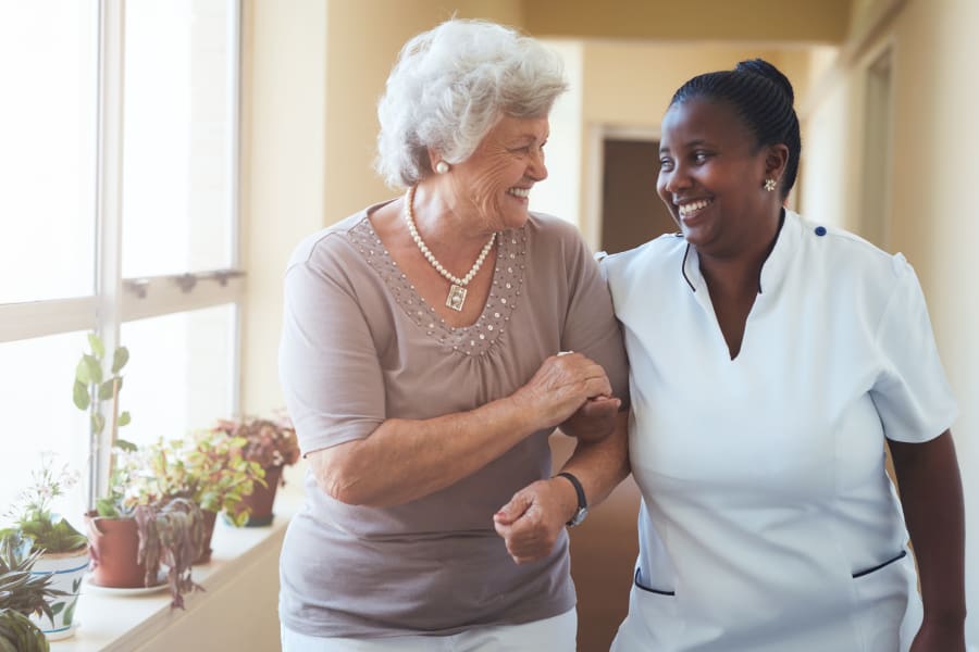 A resident walking with a CNA at Americare Senior Living