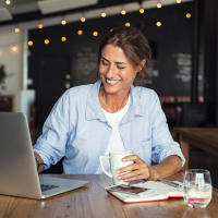 A woman sitting and using her laptop while holding a cup of coffee at Heritage at Riverstone in Canton, Georgia