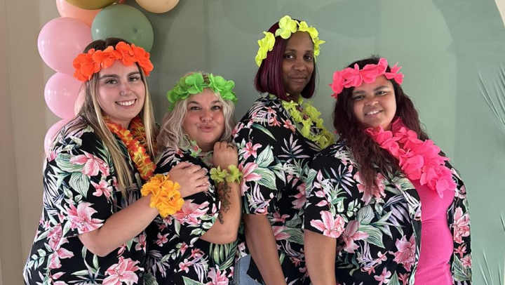 Four workers dress up in matching Hawaiian print shirts and leis for a luau