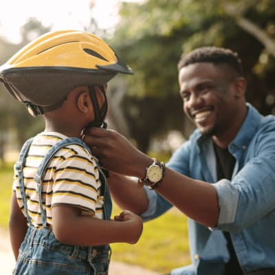 Father fastening his son's bike helmet to teach him to ride near Pointe at Northern Woods in Columbus, Ohio