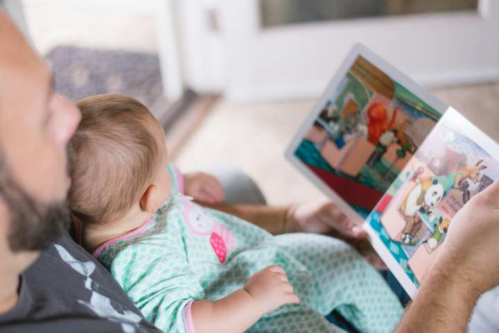 a father reads a story book to a baby on his lap