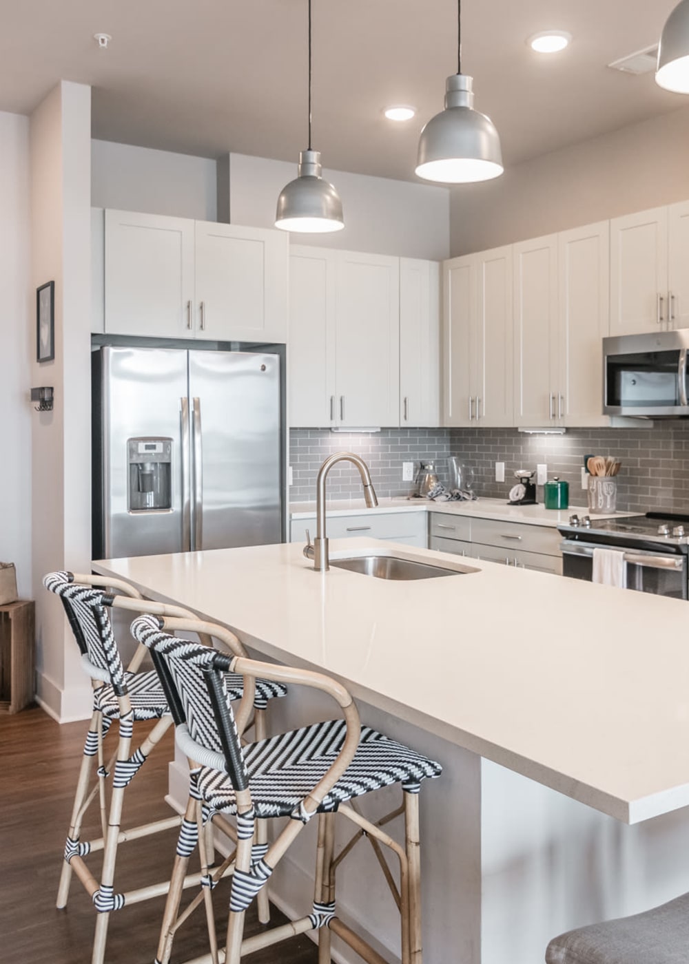 One-Bedroom Apartments in Capital View, TN - The Guthrie North Gulch - Kitchen with White Cabinetry, Hanging Lights Over the Kitchen Island, Stainless Steel Appliances, White Counters, Grey Tile Backsplash, and Luxury Hardwood-Style Flooring