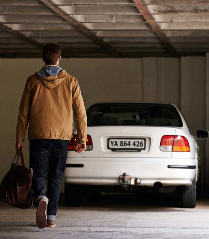 Man walking with a bag towards a parked white car in a garage at Jordache Park Apartments in Spencerport, New York