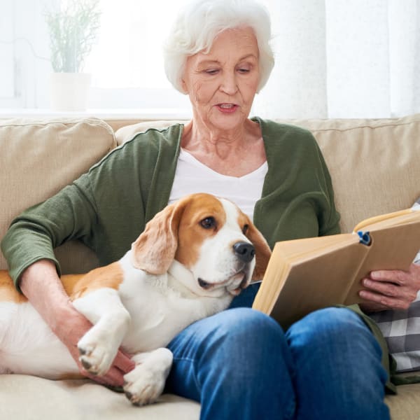 Resident reading a book while holding her pet dog at Pacifica Senior Living Oakland Heights in Oakland, California