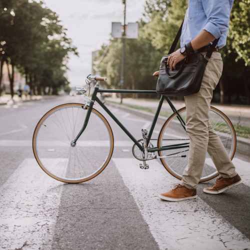 Man walking his bike across a crosswalk on his way to work near Seapointe Villas in Costa Mesa, California